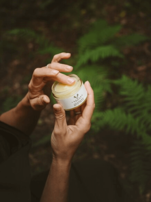 Žena v severské přírodě nanáší balzám Lapland Cosmetics na ruku – moment čisté, přírodní péče o pleť v zimním lesním prostředí